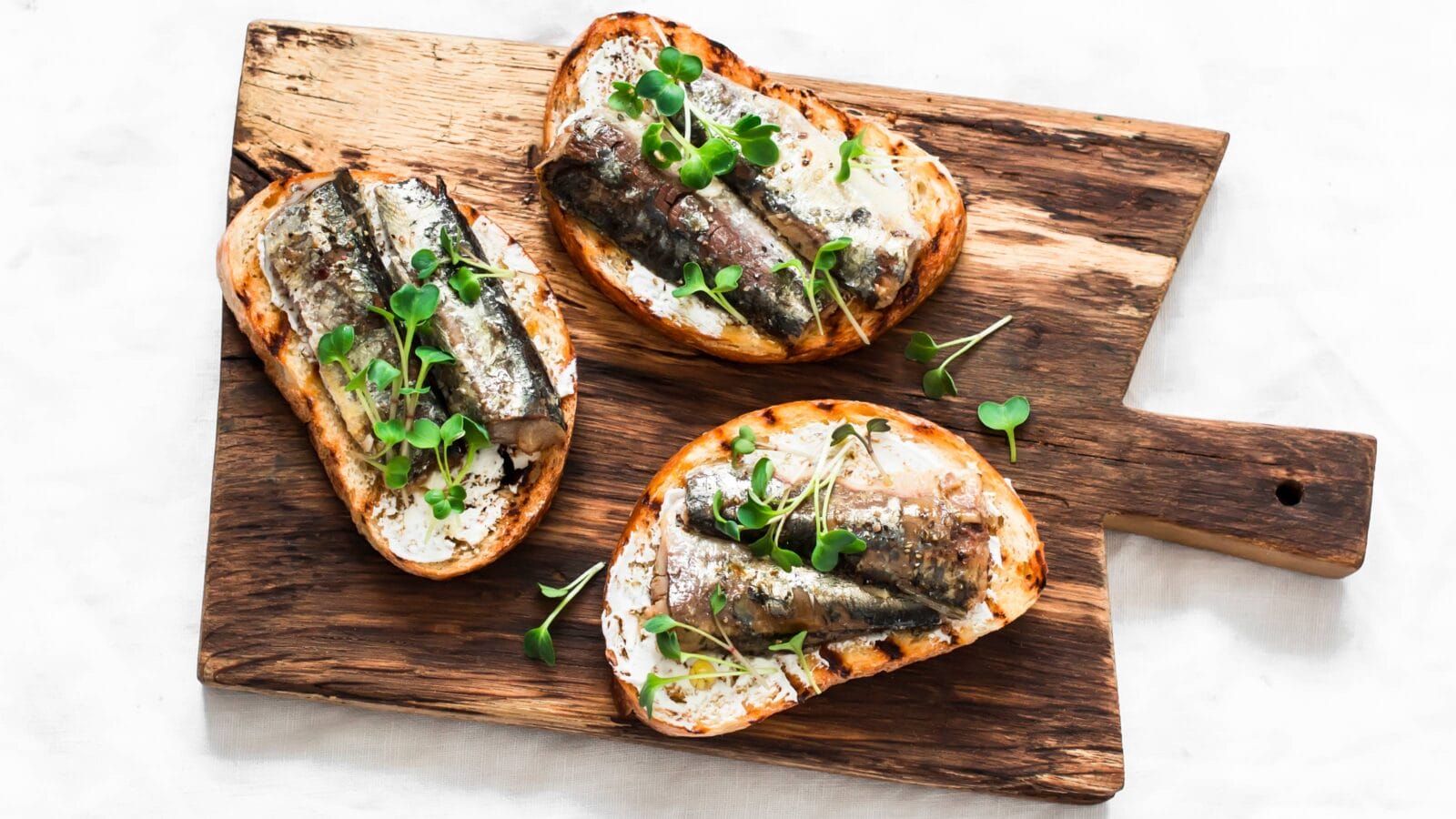 Grilled bread sardines micro greens sandwiches on a rustic cutting board