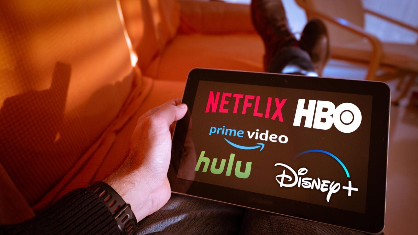 Man holds a tablet with Netflix hulu, amazon video, HBO and Disney+ logos on screen.