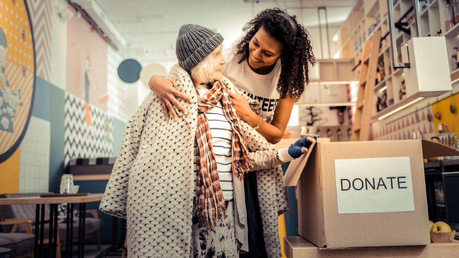 Nice joyful woman smiling while giving her old coat to a pleasant aged woman