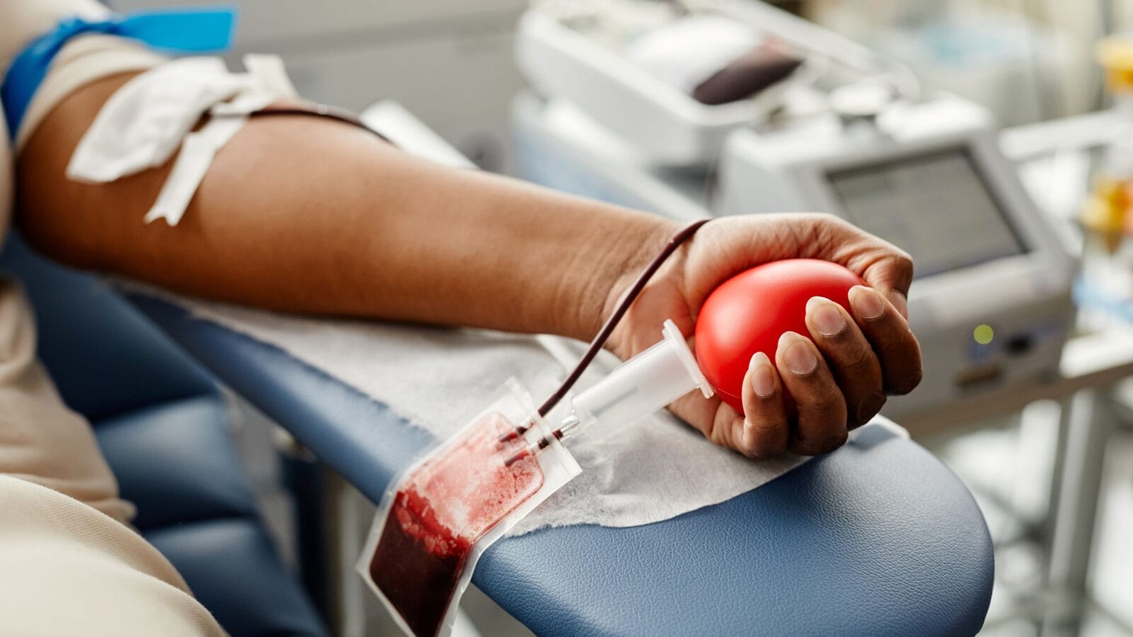 Closeup of black woman donating blood focus on hand holding red ball with tubing, copy space