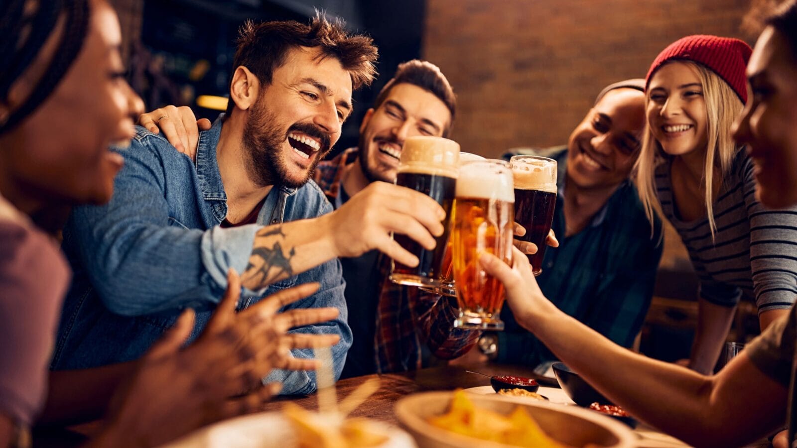 Multiracial group of happy friends having fun while toasting with beer in a bar