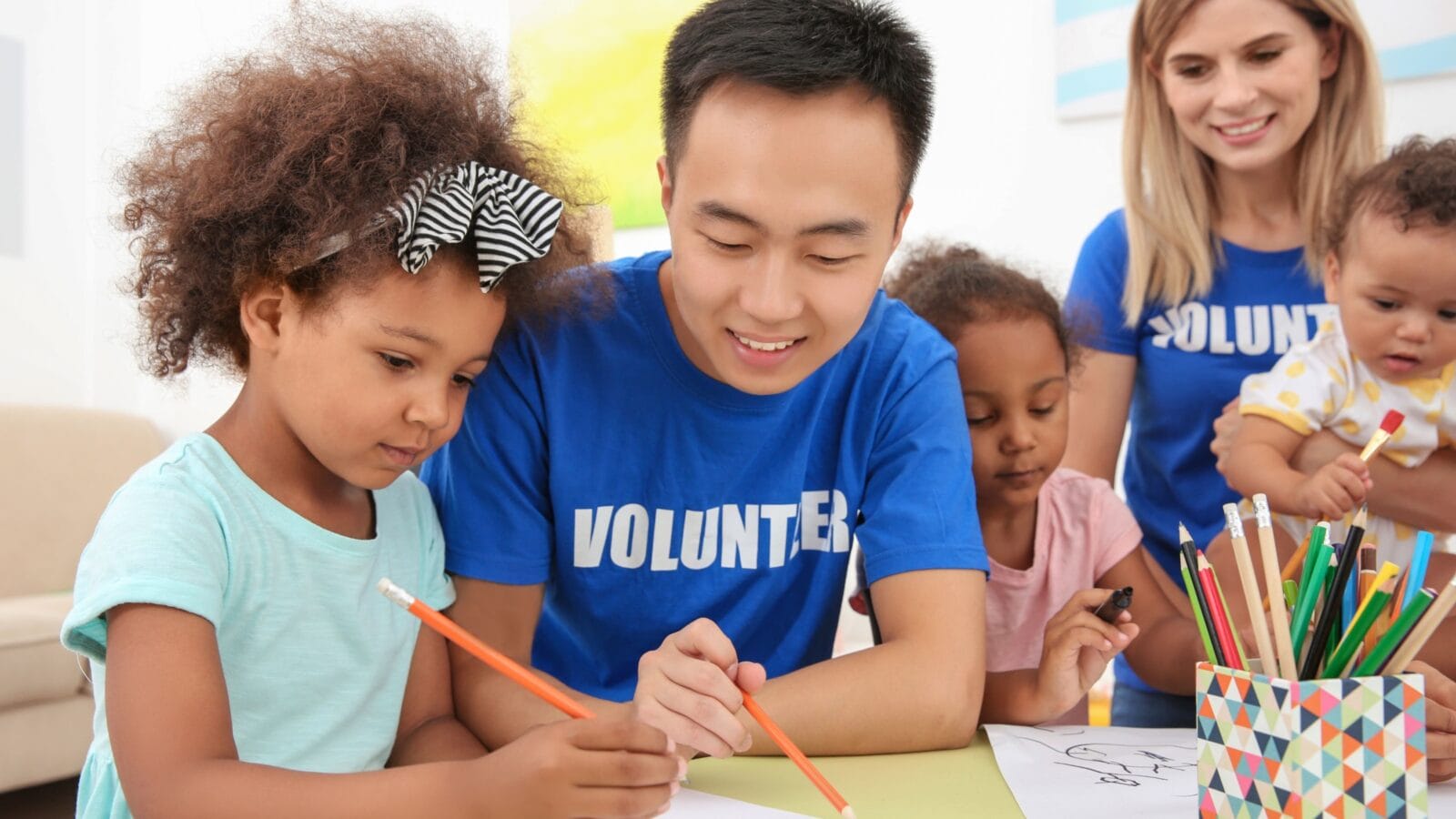 Young male volunteer drawing with little children at table