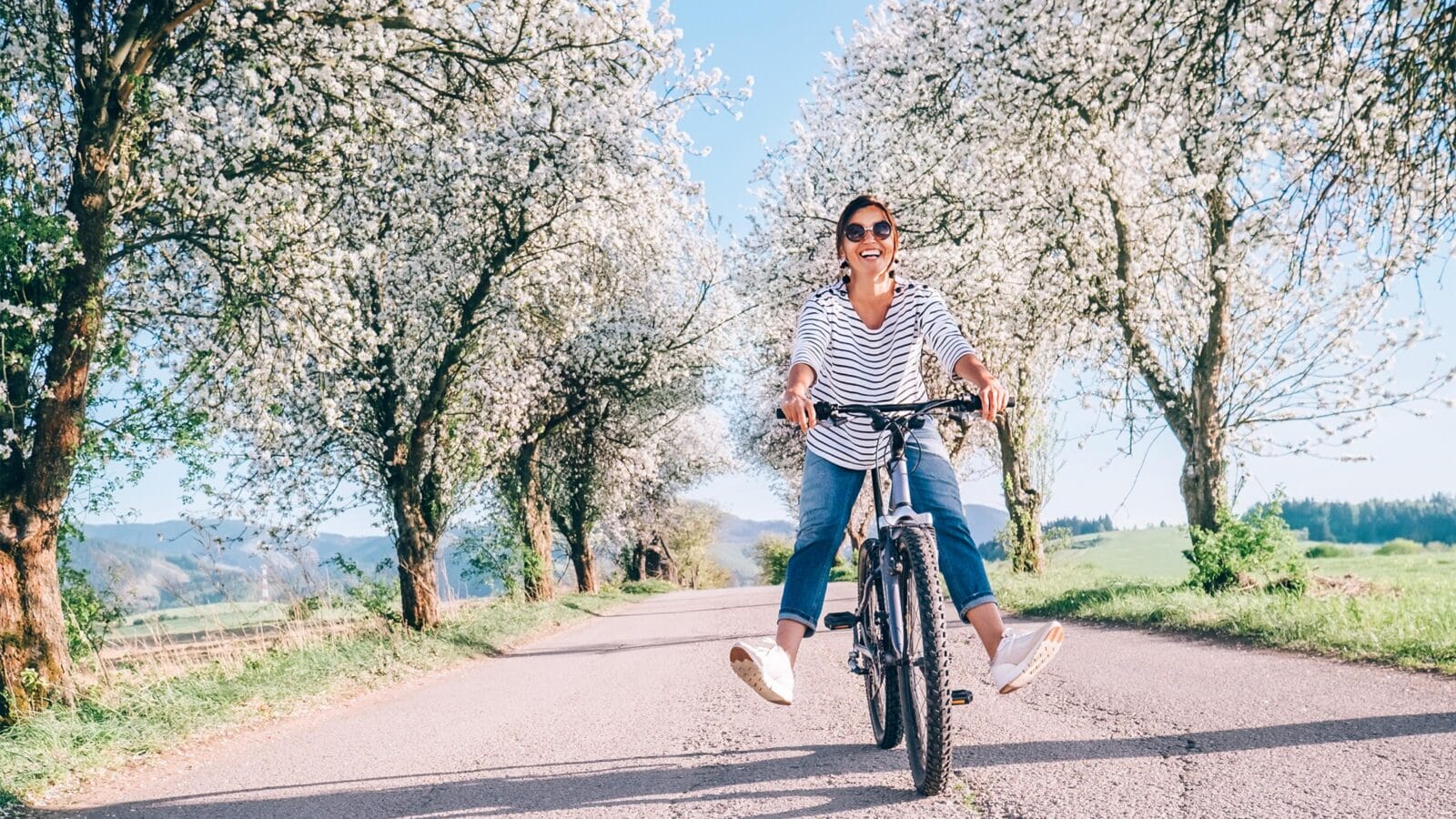 Happy smiling woman rides a bicycle on the country road under the apple blossom trees