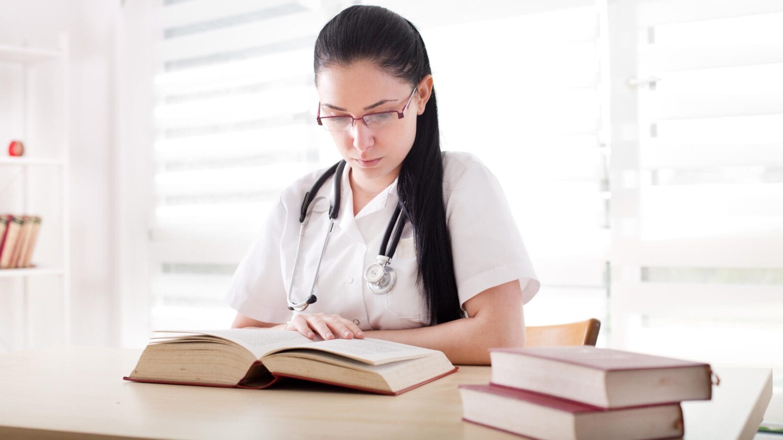 Young girl, student of medicine studying and researching books at desk in the office