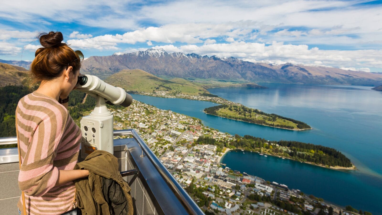 Young adult woman enjoy a stunning view of Queenstown through the binocular from view point of the Skyline Gondola
