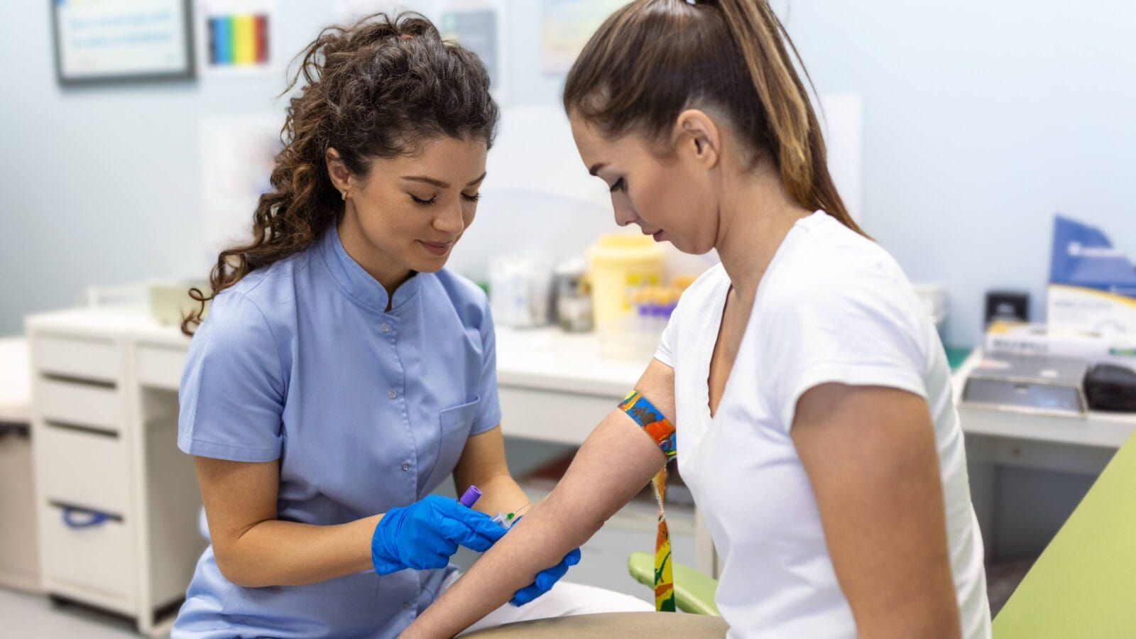Preparation for blood test with pretty young woman by female doctor medical uniform on the table in white bright room.