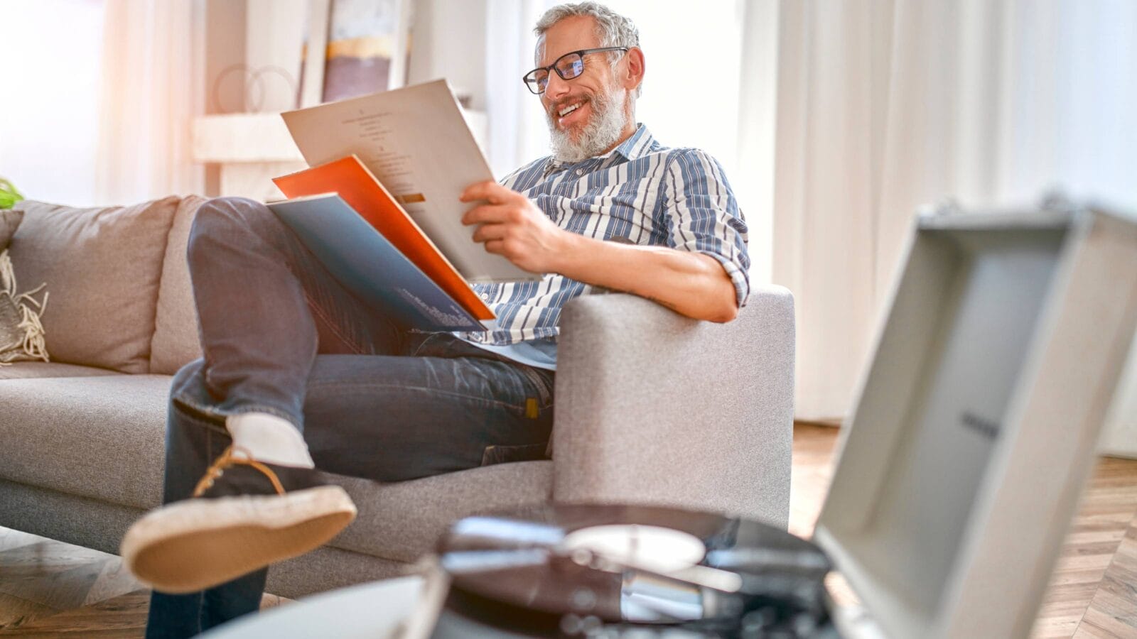 A mature man sits on the couch at home, relaxes, enjoys life and listens to vinyl records on a music player.
