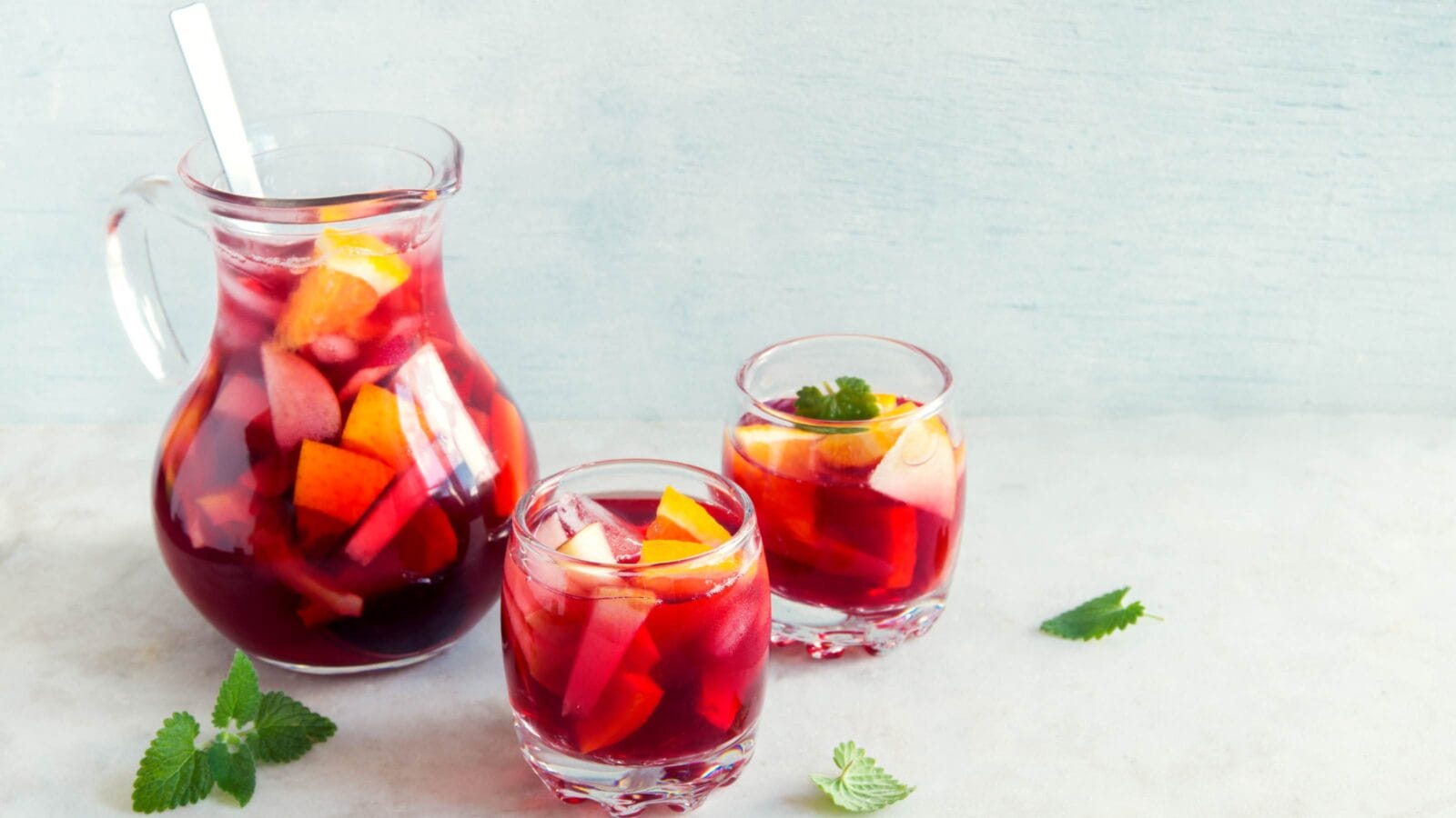 Red wine sangria or punch with fruits, mint and ice in glasses.
