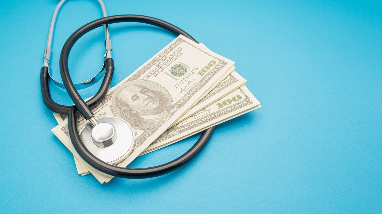 Top view of a stethoscope and US dollar banknotes on a blue background.