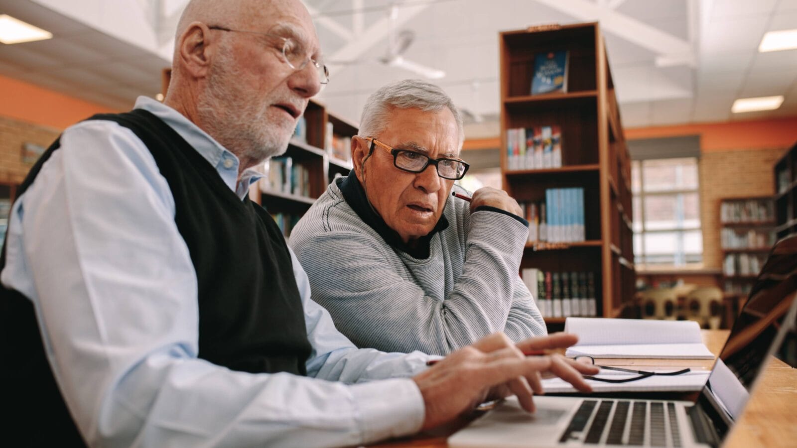 Senior men sitting in a library and learning their courses on a laptop.