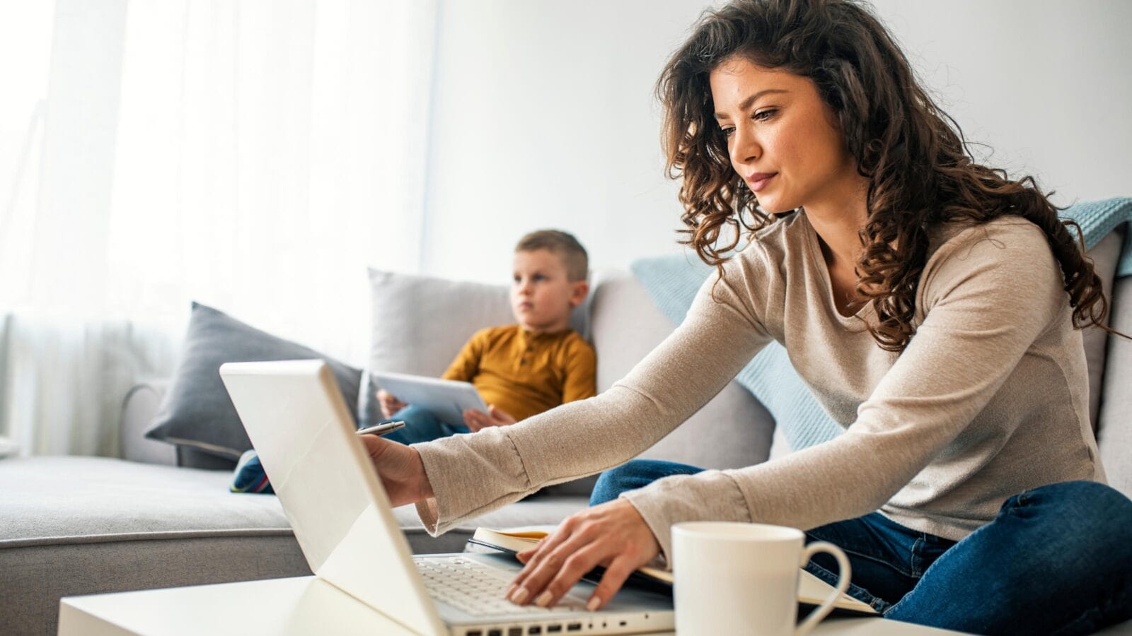 Smiling mom working at home with her child on the sofa while writing an email.