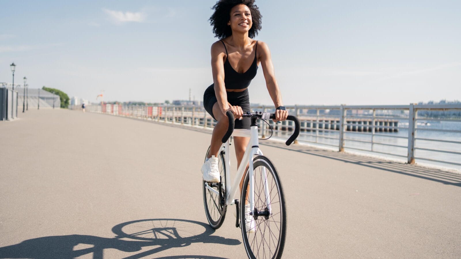 Happy smiling young woman curly-haired contented activity road bike riding in a sports black suit.