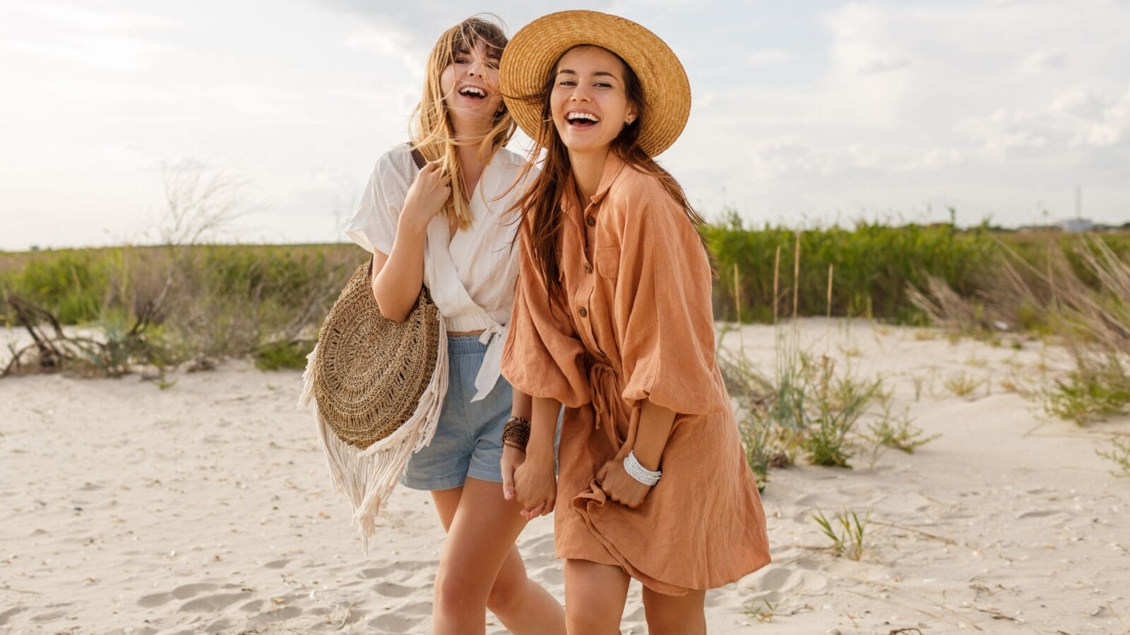 Two pretty sister girls posing on the beach, vacation mood, crazy positive feeling, summer trendy clothes and straw hat.