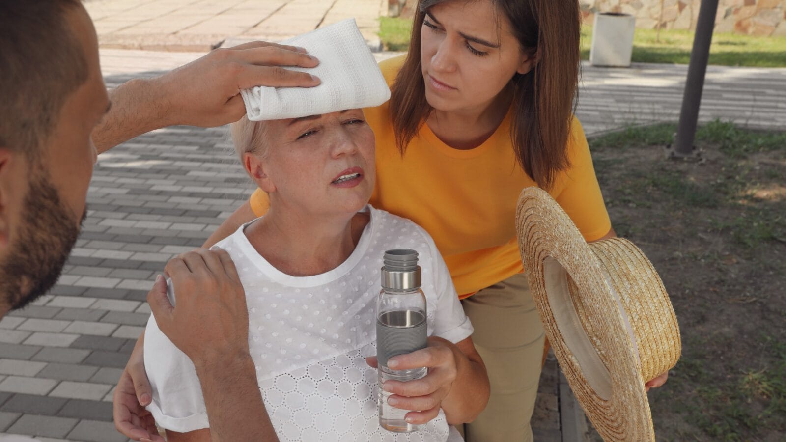 People helping mature woman on city street. Suffering from heat stroke